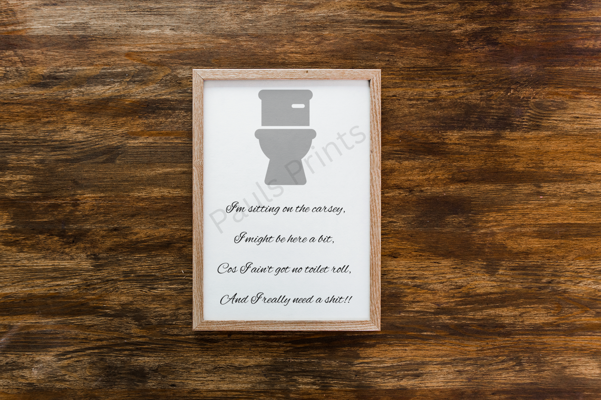 Funny framed bathroom wall art with a grey toilet icon and cheeky rhyme, placed on a rustic wooden surface.