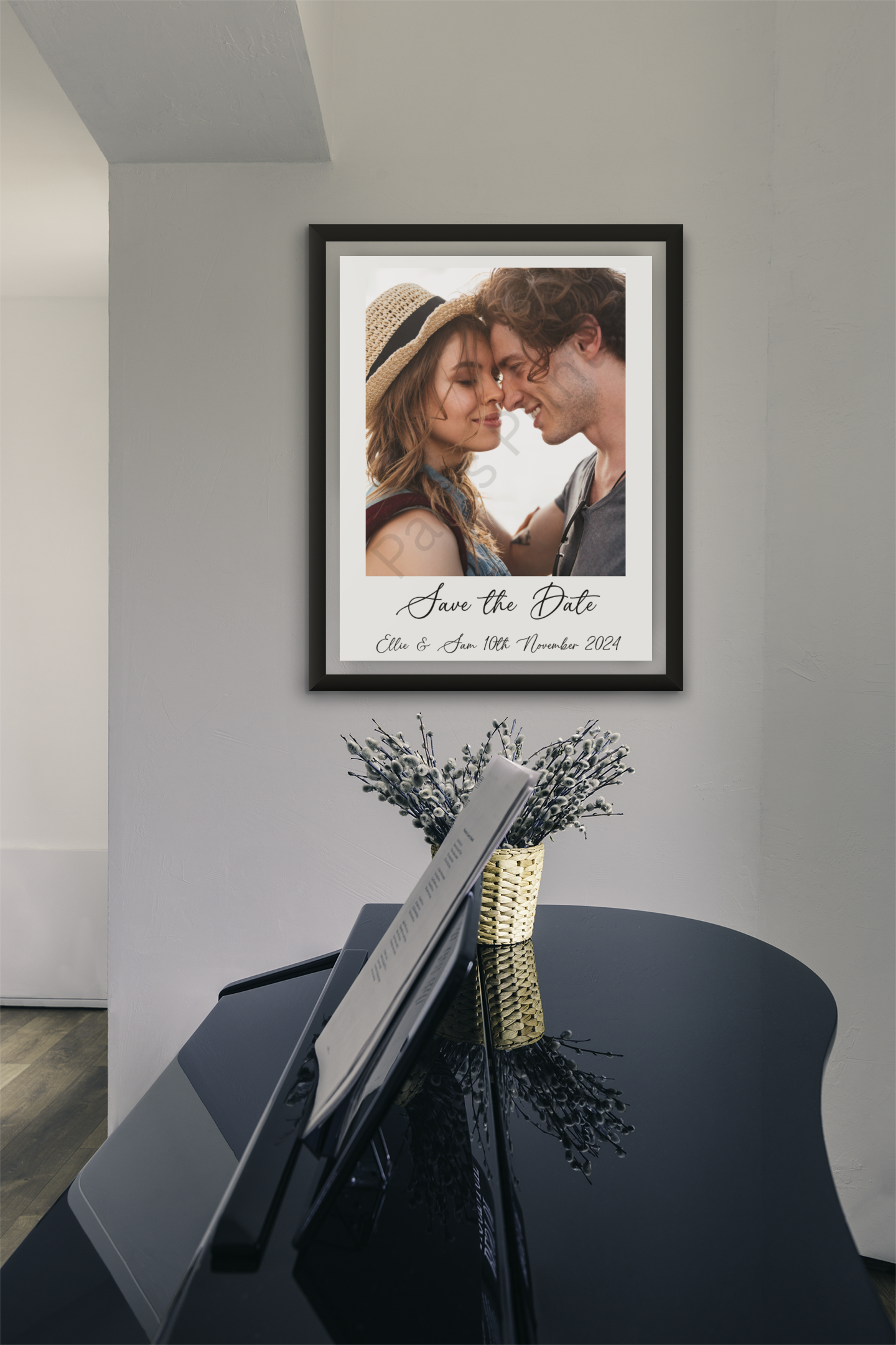 Framed save the date print with a couple’s photo and wedding date, hanging above a piano with a vase of flowers.