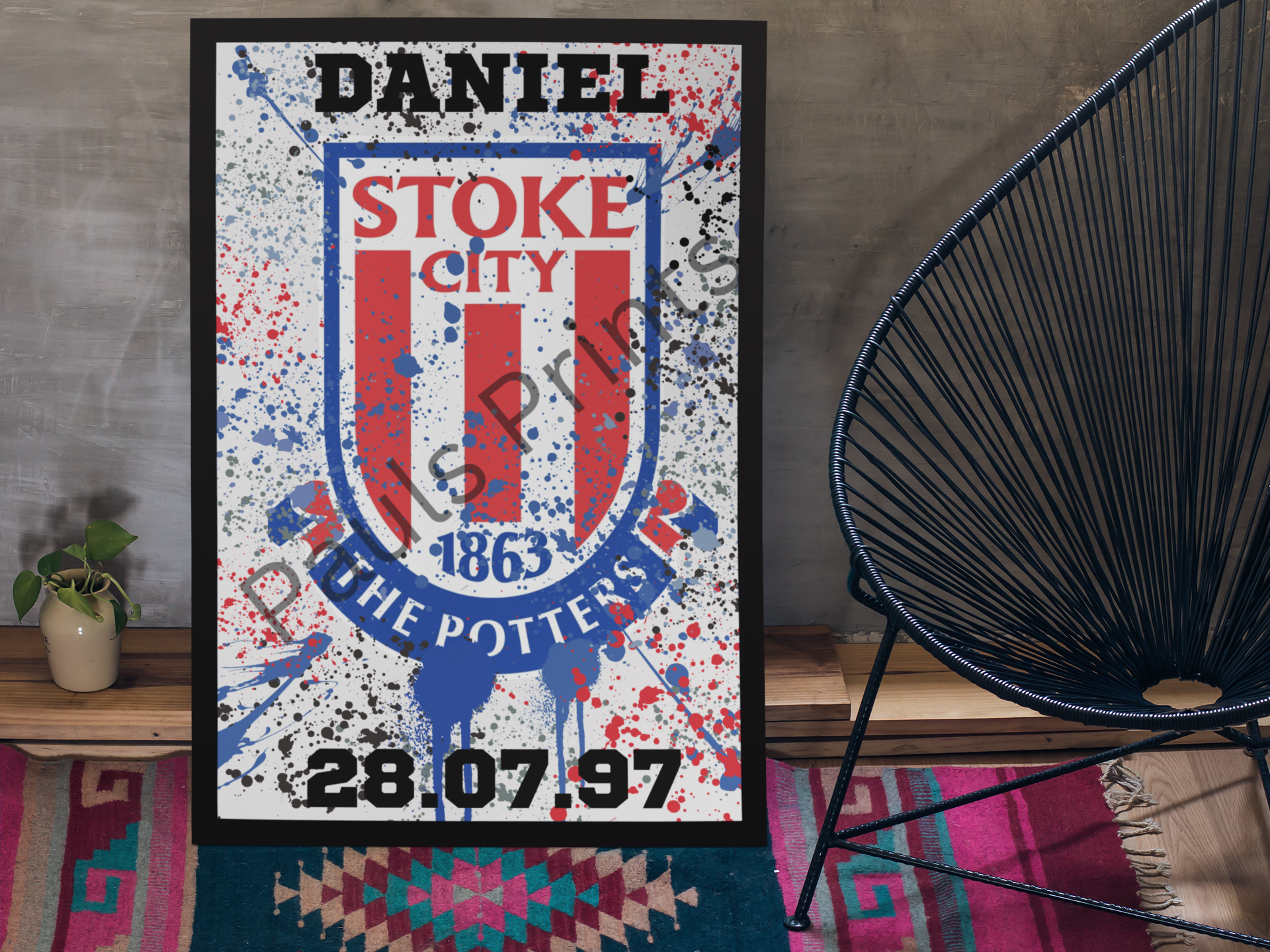 Framed personalised football print on grey wall beside modern chair and small plant.