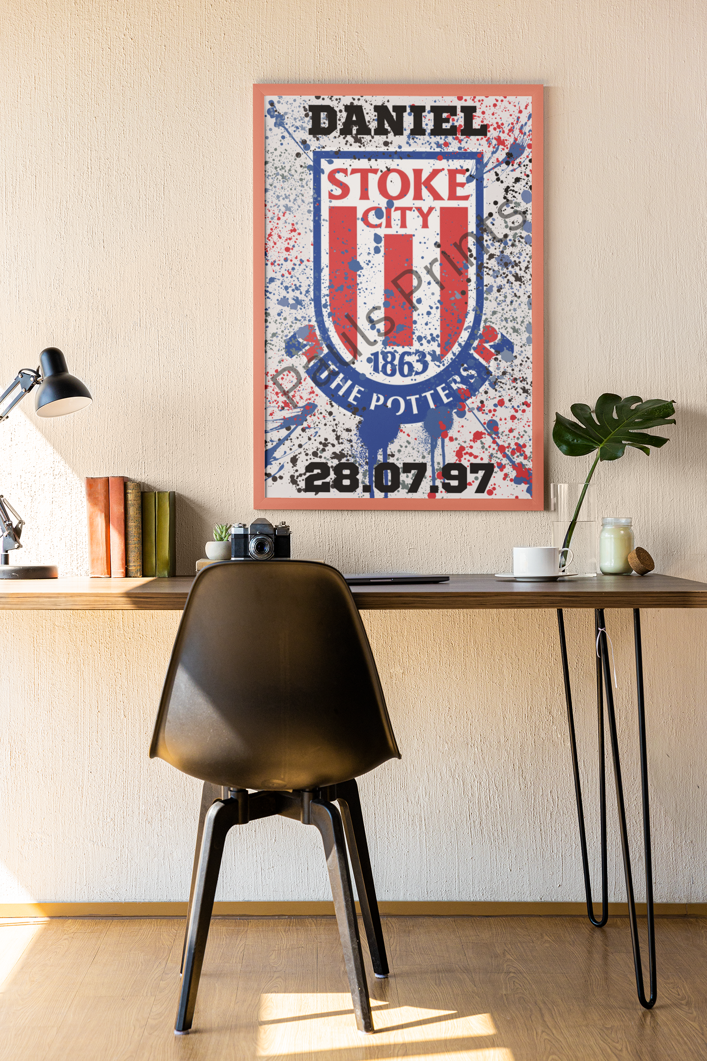 Framed Stoke City wall art with custom name and date, hanging above wooden desk with books and lamp.