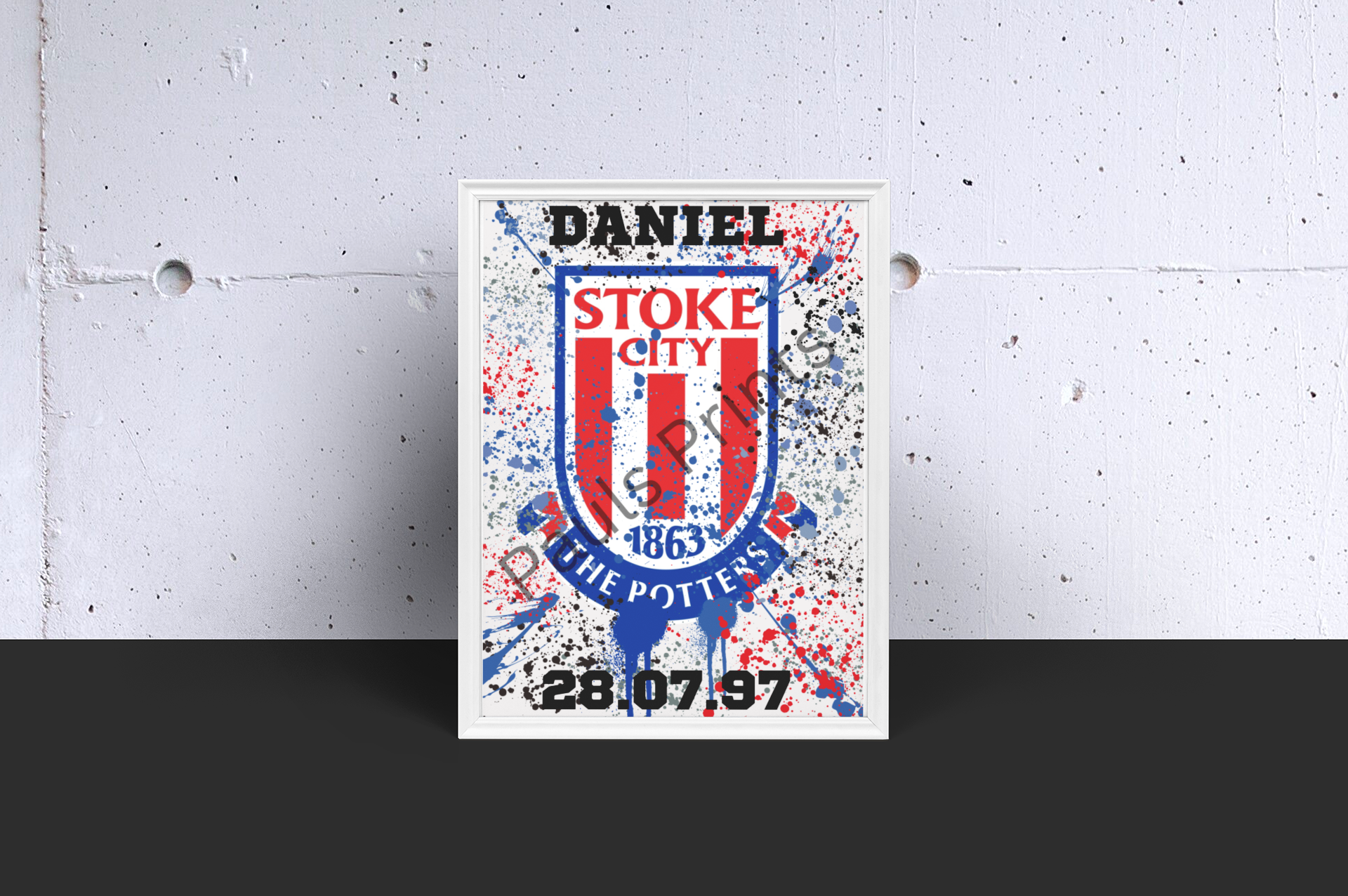 Framed Stoke City FC print with custom text and splatter effects, leaning against concrete wall.