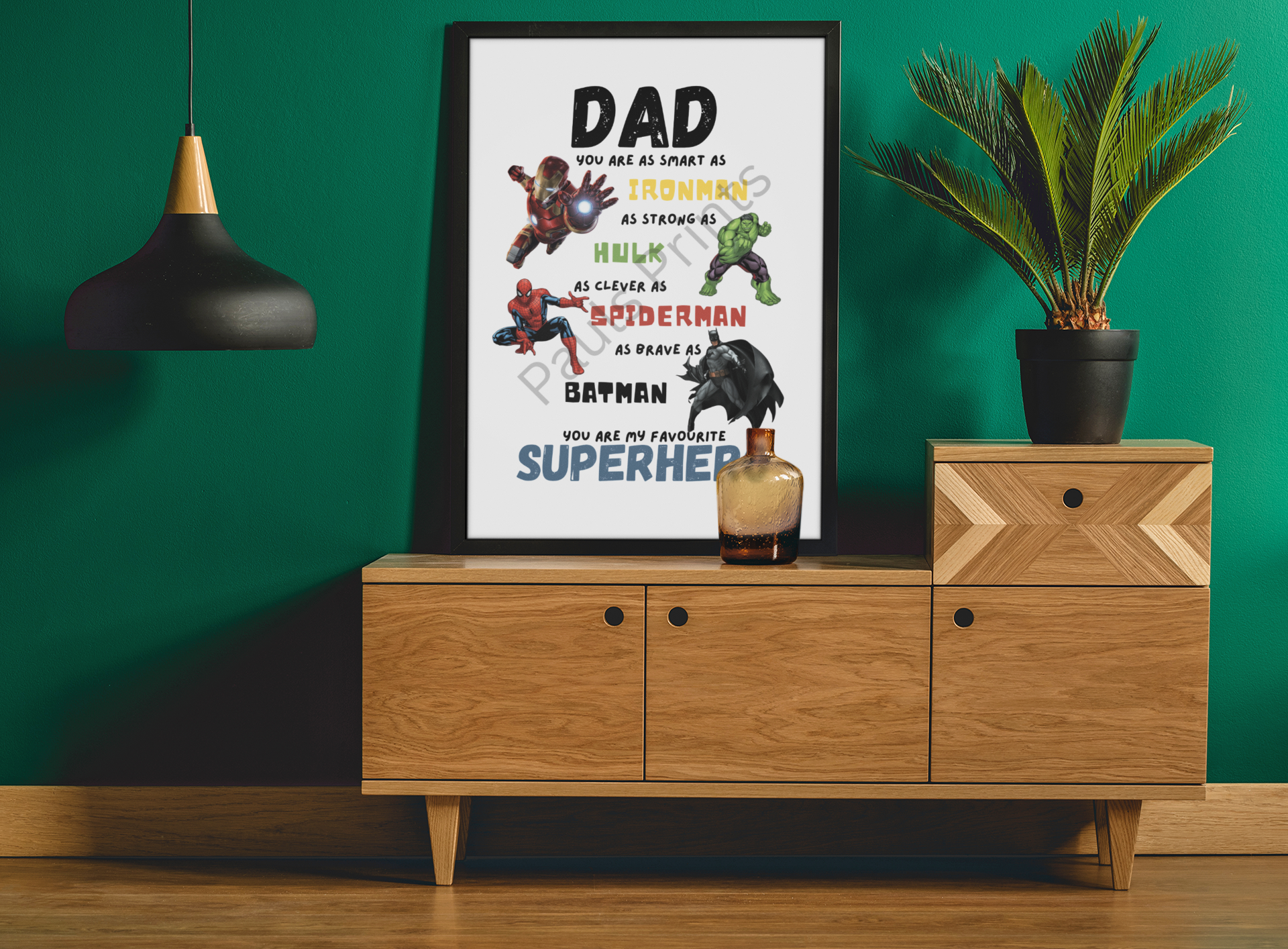 Bold superhero dad quote print framed on green wall above a wooden sideboard with a lamp and indoor plant.