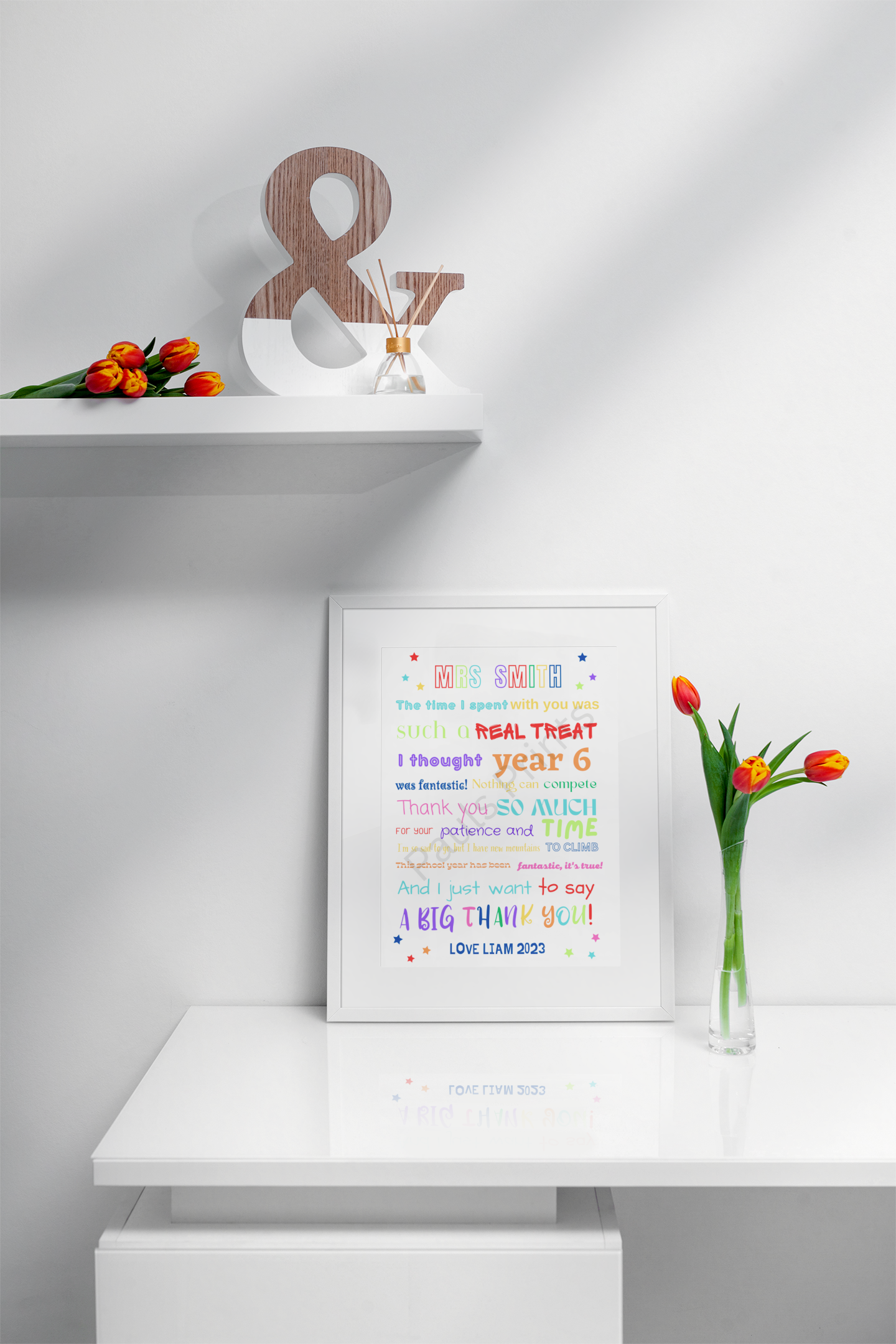 Bright teacher thank you poem print in white frame placed under a shelf with orange tulips and wood ampersand decor.