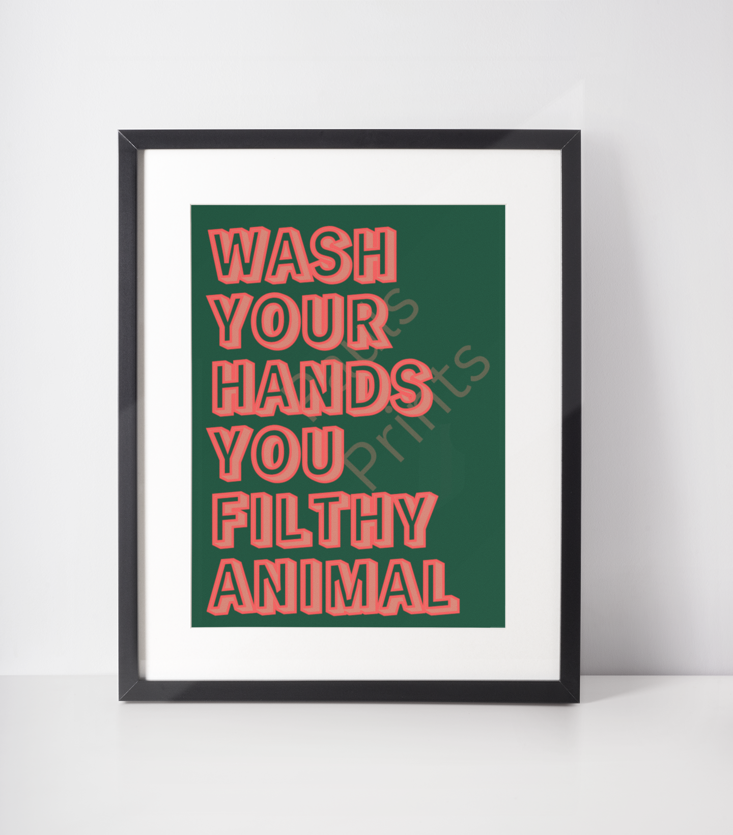 Framed print with bold red and pink block lettering reading “Wash Your Hands You Filthy Animal” on a dark green background, displayed upright against a white wall.