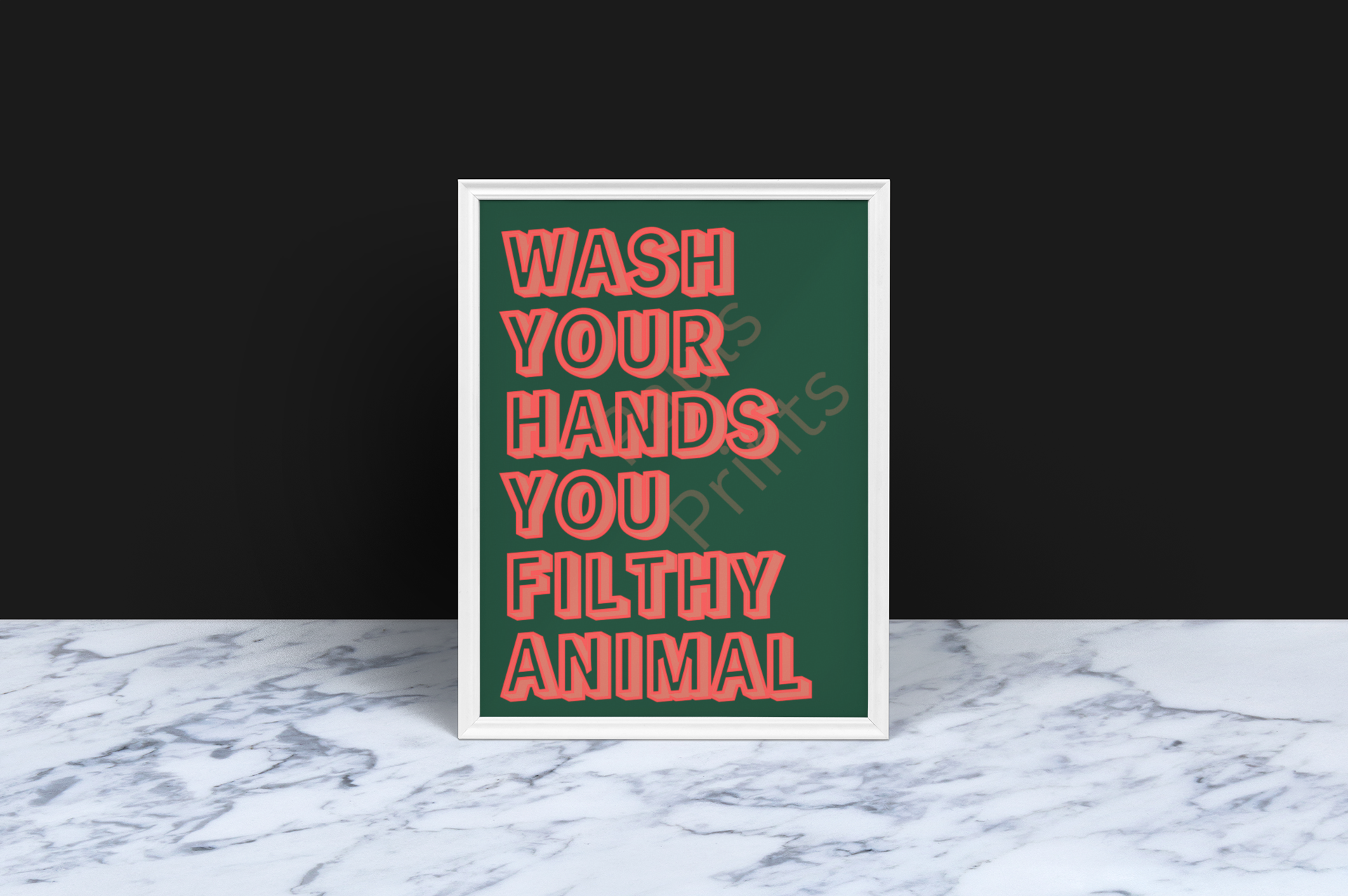 Large framed print in a black frame with red block letters on a green background reading “Wash Your Hands You Filthy Animal,” hung on a textured grey wall with pendant lighting and plants nearby.