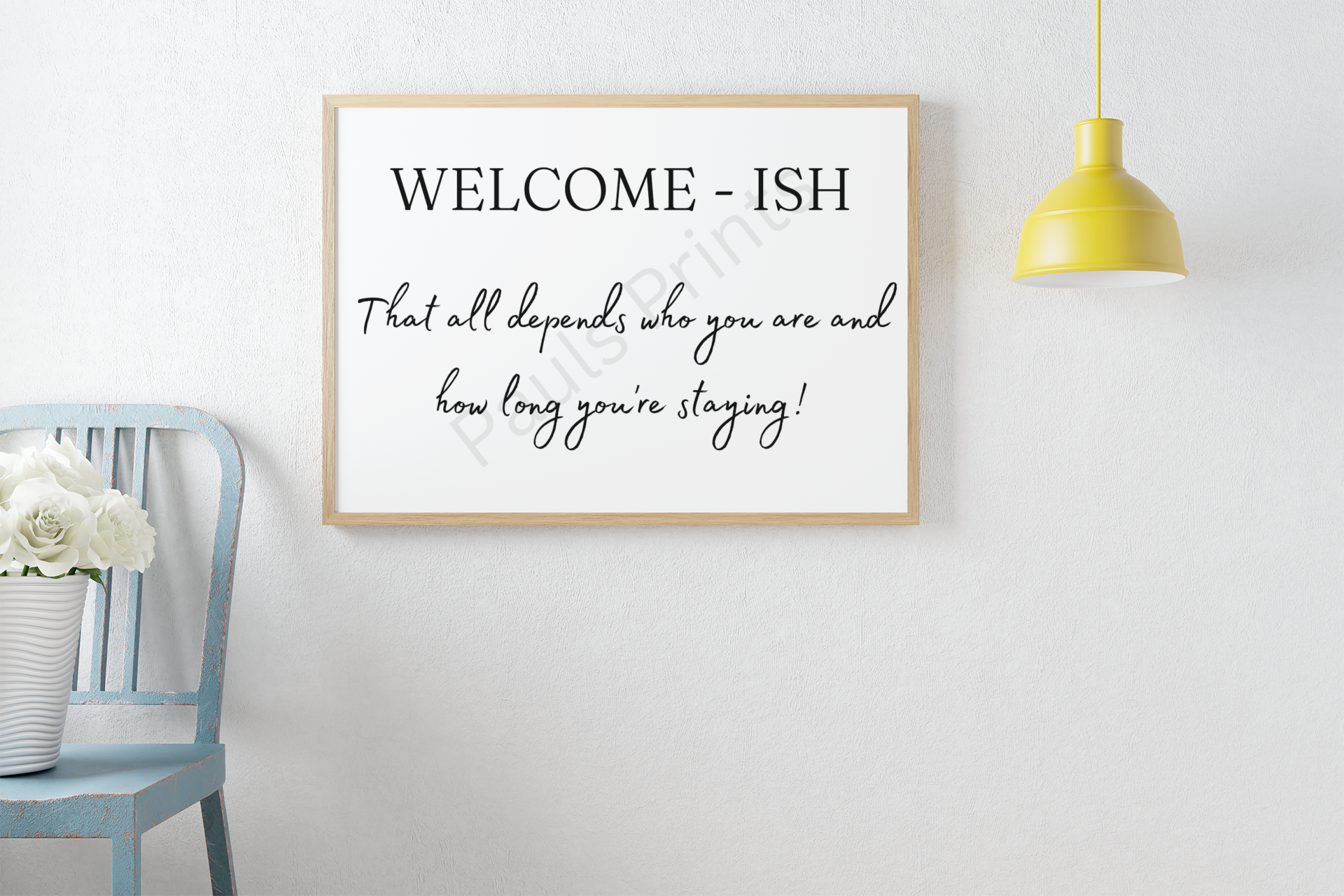 Humorous “Welcome-ish” framed print with the text “That all depends who you are and how long you’re staying!”, displayed above a vintage blue chair with white flowers.