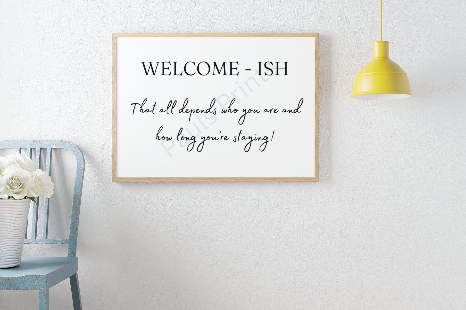 Light wood framed wall print saying "Welcome-ish – That all depends who you are and how long you’re staying!" next to a blue distressed chair with white flowers and a yellow hanging lamp.