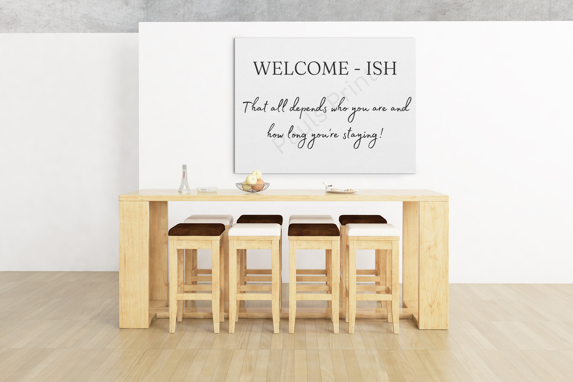 Framed wall art with the phrase "Welcome-ish – That all depends who you are and how long you’re staying!" displayed above a light wooden dining table and stools.